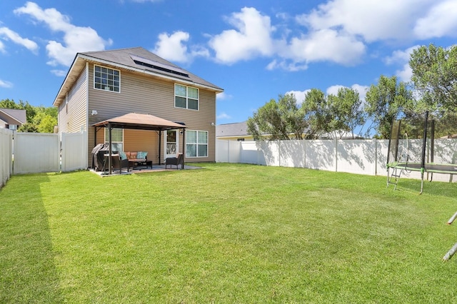 rear view of house with solar panels, a trampoline, a gazebo, a yard, and a patio area