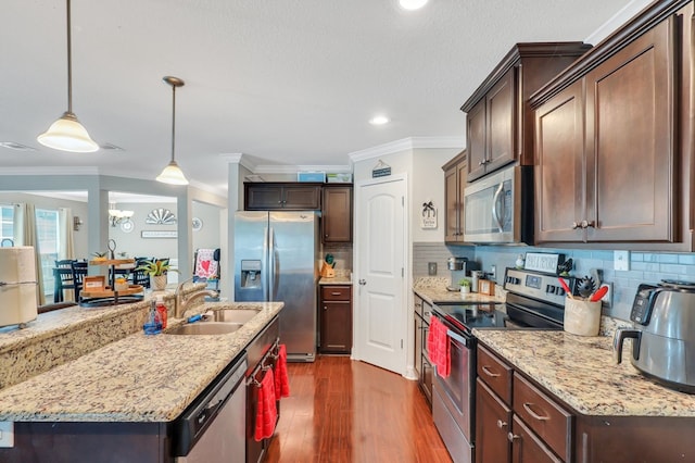 kitchen featuring ornamental molding, stainless steel appliances, sink, decorative light fixtures, and an island with sink