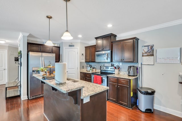 kitchen with appliances with stainless steel finishes, a kitchen breakfast bar, dark hardwood / wood-style floors, hanging light fixtures, and an island with sink