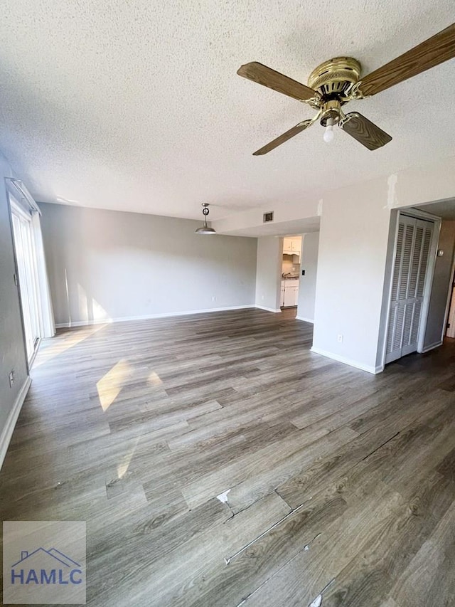 unfurnished living room featuring dark hardwood / wood-style floors, ceiling fan, and a textured ceiling