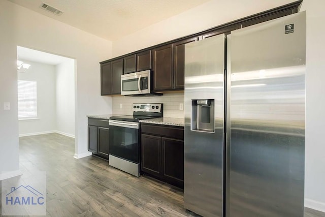 kitchen with an inviting chandelier, wood-type flooring, decorative backsplash, appliances with stainless steel finishes, and dark brown cabinetry