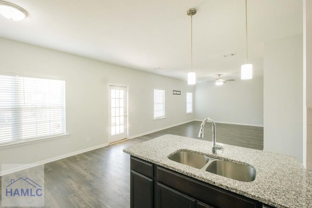 kitchen with dark wood-type flooring, light stone counters, sink, and hanging light fixtures