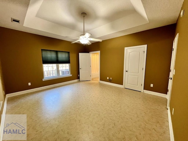 unfurnished bedroom featuring ceiling fan, a textured ceiling, and a tray ceiling