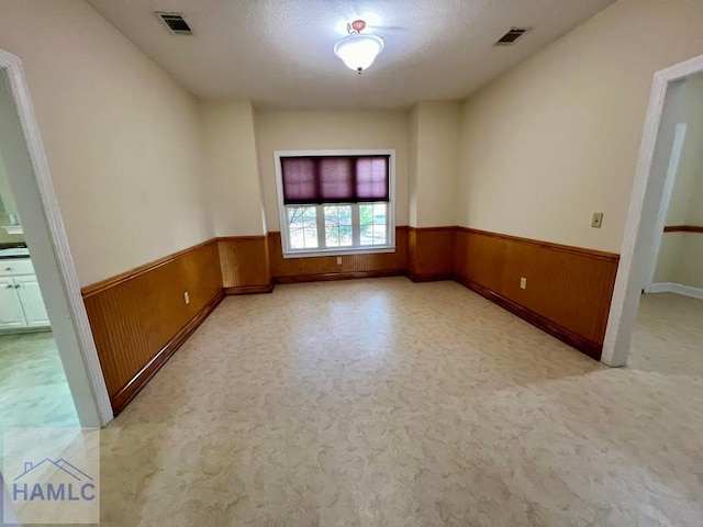 empty room with wooden walls, light colored carpet, and a textured ceiling