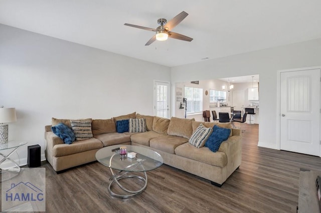 living room featuring ceiling fan with notable chandelier, baseboards, and dark wood-style flooring