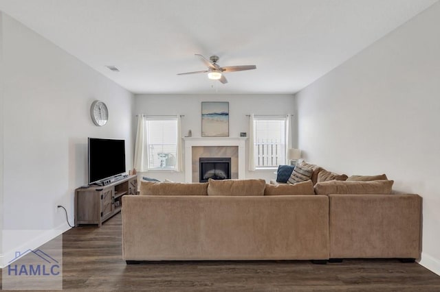 living room featuring visible vents, a ceiling fan, a tiled fireplace, dark wood-style floors, and baseboards