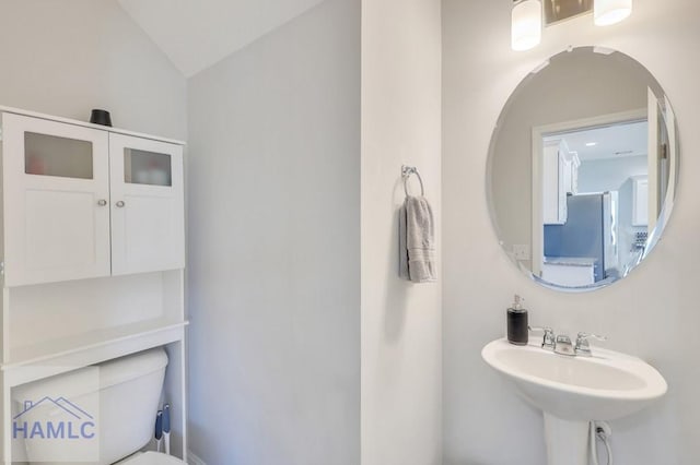 half bathroom with a sink, lofted ceiling, and toilet