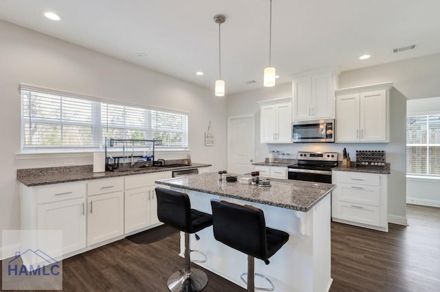 kitchen featuring visible vents, a kitchen island, dark wood finished floors, stainless steel appliances, and white cabinets