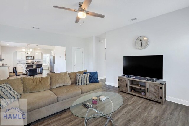 living room with visible vents, ceiling fan with notable chandelier, baseboards, and wood finished floors