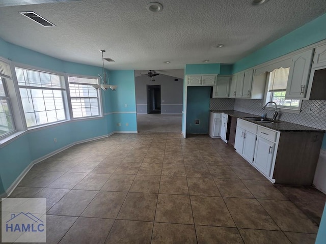kitchen with decorative backsplash, visible vents, dark countertops, white cabinetry, and a sink