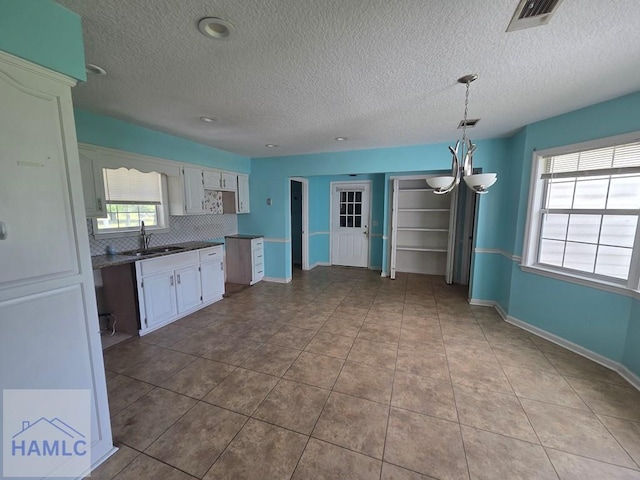 kitchen with a sink, a chandelier, tasteful backsplash, visible vents, and white cabinets