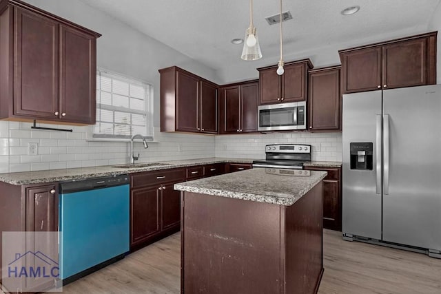 kitchen with a kitchen island, decorative light fixtures, sink, stainless steel appliances, and light hardwood / wood-style flooring