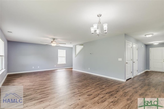 empty room with a chandelier, a ceiling fan, dark wood-type flooring, and baseboards