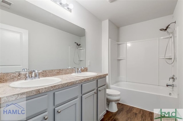 bathroom with toilet, wood finished floors, double vanity, and bathtub / shower combination