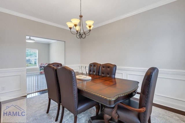 dining space featuring an inviting chandelier, wainscoting, crown molding, and a decorative wall