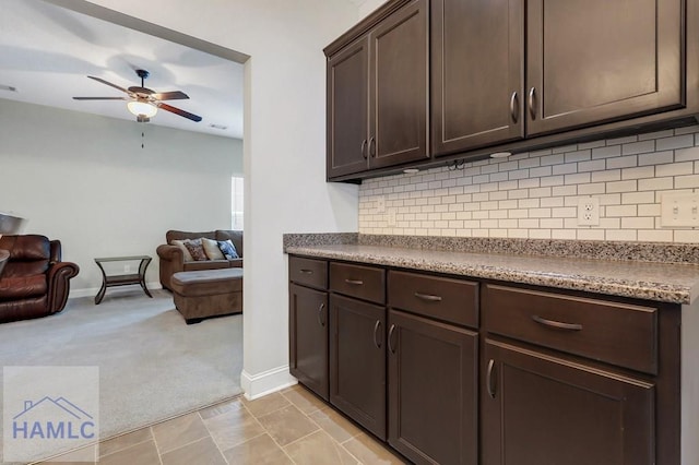 kitchen with dark brown cabinetry, baseboards, open floor plan, ceiling fan, and light colored carpet