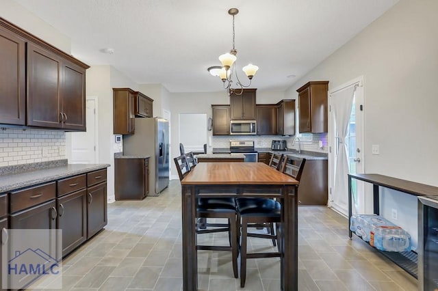 kitchen with appliances with stainless steel finishes, backsplash, a notable chandelier, and dark brown cabinets