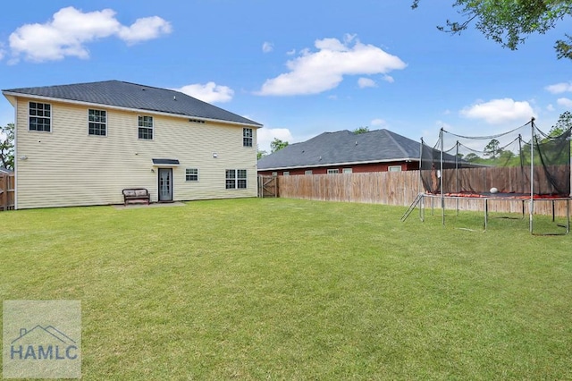 back of property with a lawn, a fenced backyard, and a trampoline