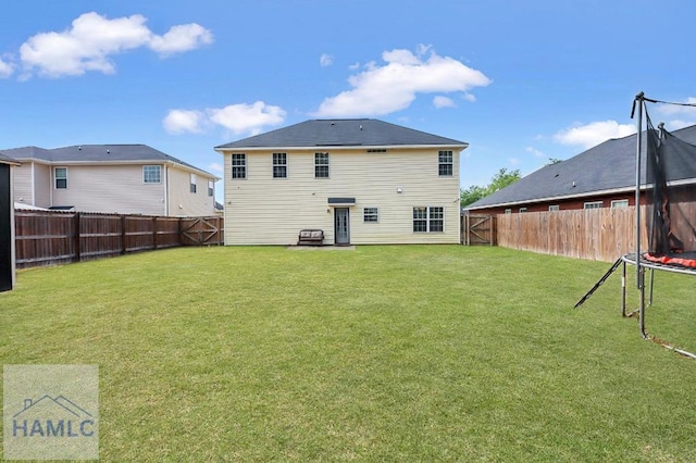 rear view of house with a yard, a fenced backyard, and a trampoline