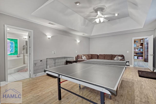 playroom with a raised ceiling, light hardwood / wood-style flooring, ceiling fan, and built in shelves