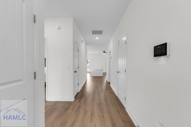 corridor with light wood-style flooring, visible vents, and baseboards
