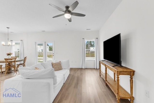 living room featuring light wood-type flooring, baseboards, visible vents, and ceiling fan with notable chandelier