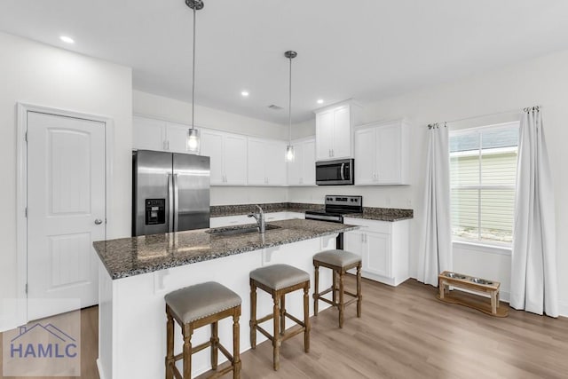 kitchen with stainless steel appliances, an island with sink, a sink, and white cabinetry