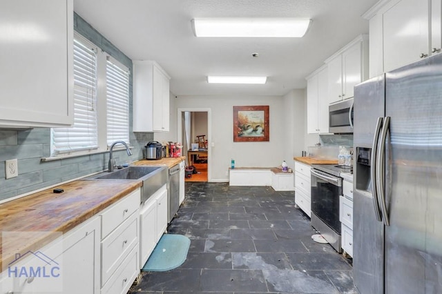 kitchen with butcher block countertops, sink, white cabinetry, and stainless steel appliances