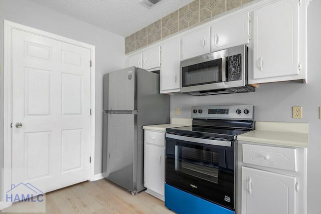 kitchen featuring appliances with stainless steel finishes, light countertops, light wood finished floors, white cabinetry, and a textured ceiling