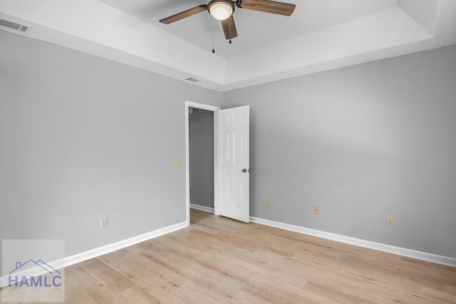 unfurnished room with light wood finished floors, ceiling fan, a tray ceiling, visible vents, and baseboards