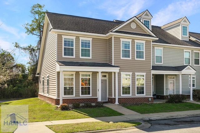 view of property featuring a front yard, brick siding, and roof with shingles