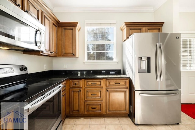 kitchen with stainless steel appliances, dark stone counters, brown cabinetry, and crown molding