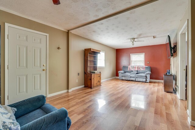 living area featuring light wood-style flooring, a textured ceiling, baseboards, and a ceiling fan