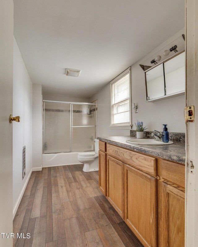 full bathroom with hardwood / wood-style floors, vanity, bath / shower combo with glass door, and toilet