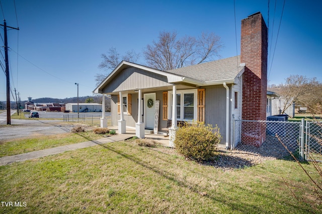 bungalow-style home with covered porch, a shingled roof, fence, a front lawn, and a chimney