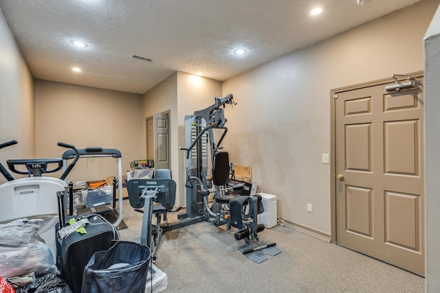 exercise area featuring light colored carpet and a textured ceiling