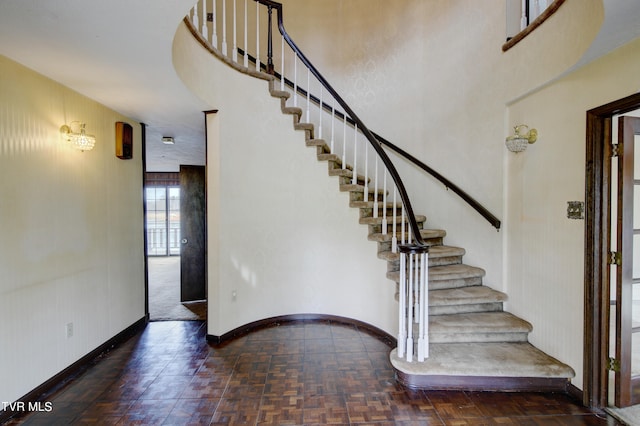 stairway featuring dark parquet flooring and a high ceiling