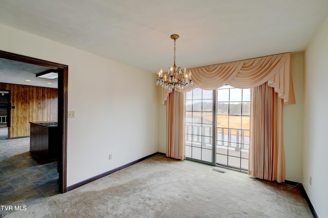 carpeted empty room with a notable chandelier and wooden walls