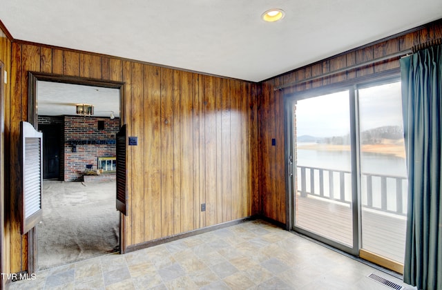 spare room with a brick fireplace, light tile flooring, wood walls, and a water view