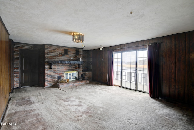 unfurnished living room with light carpet, wood walls, a brick fireplace, and a textured ceiling