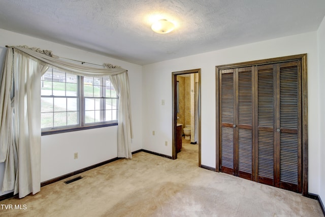 unfurnished bedroom featuring a closet, ensuite bath, a textured ceiling, and light colored carpet