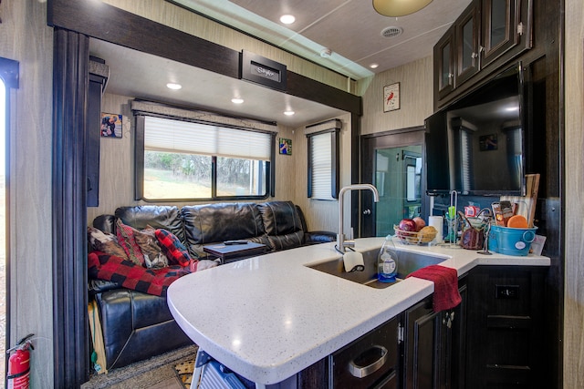 kitchen featuring dark brown cabinets, light stone counters, and sink