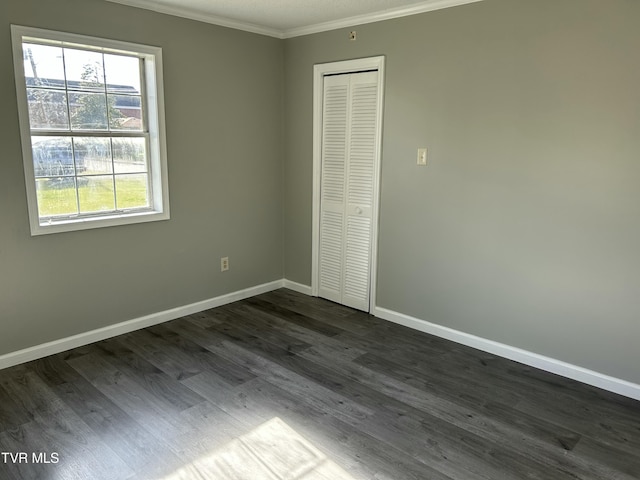 unfurnished bedroom featuring dark wood-type flooring, ornamental molding, and a closet