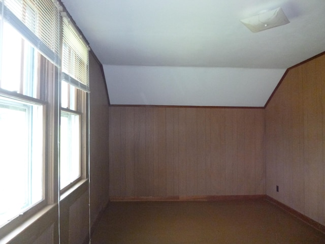 additional living space with wooden walls, dark carpet, and vaulted ceiling