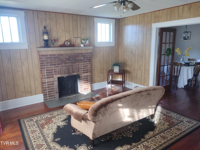 living room with wooden walls, ceiling fan, a brick fireplace, and dark wood-type flooring