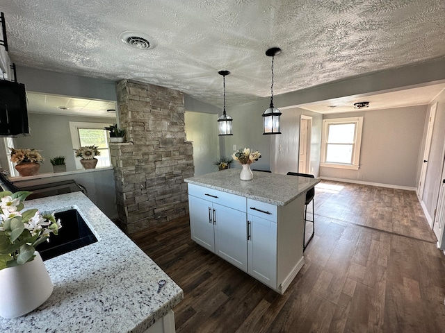 kitchen with dark hardwood / wood-style flooring, decorative light fixtures, white cabinetry, and light stone counters