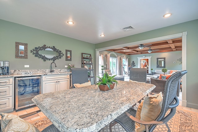 kitchen with coffered ceiling, beamed ceiling, beverage cooler, light stone countertops, and ceiling fan