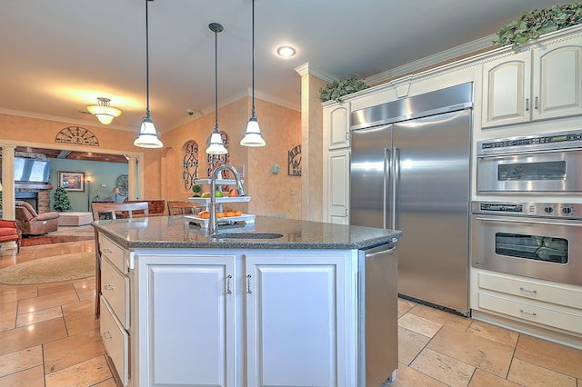 kitchen with stainless steel appliances, ornamental molding, a brick fireplace, and an island with sink