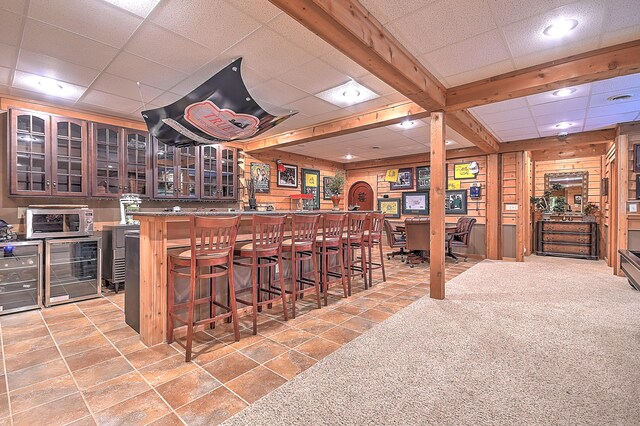 bar featuring wooden walls, a drop ceiling, wine cooler, and light tile flooring