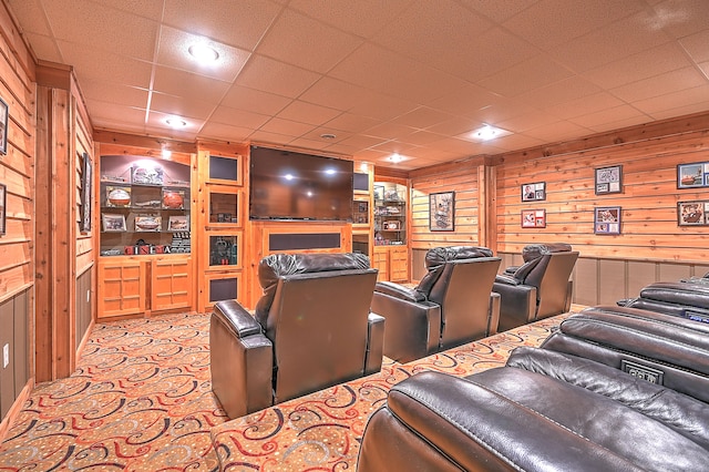 carpeted home theater room with wood walls, a paneled ceiling, and built in shelves